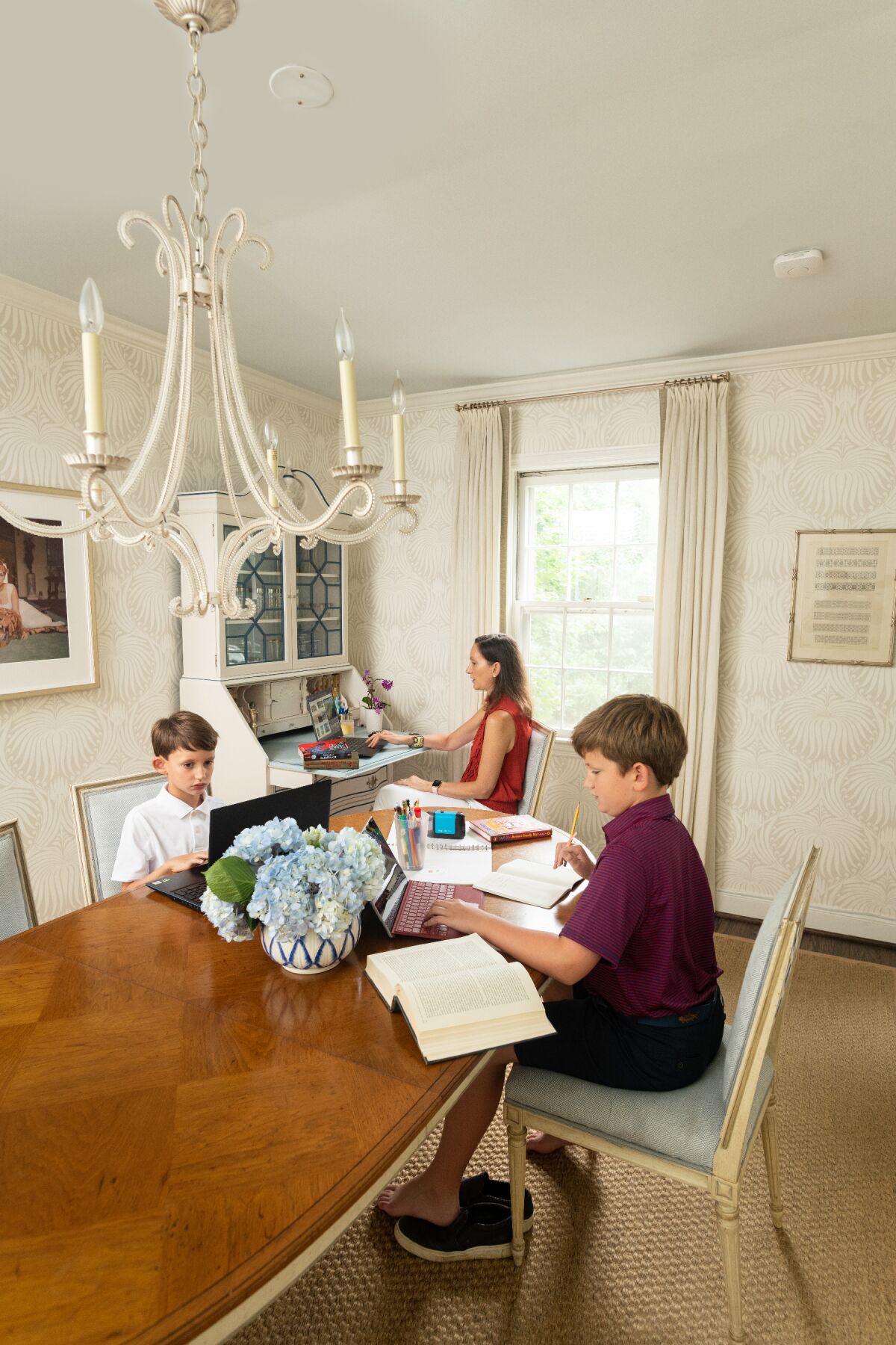 A mom works at a desk in the corner of the dining room while her two sons work on schoolwork at the table.