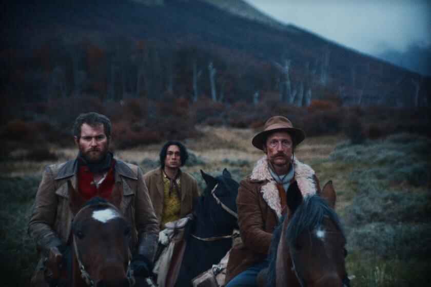 A film still shows three men in 19th century clothing on horseback in a chilly, damp, mountainous environment.