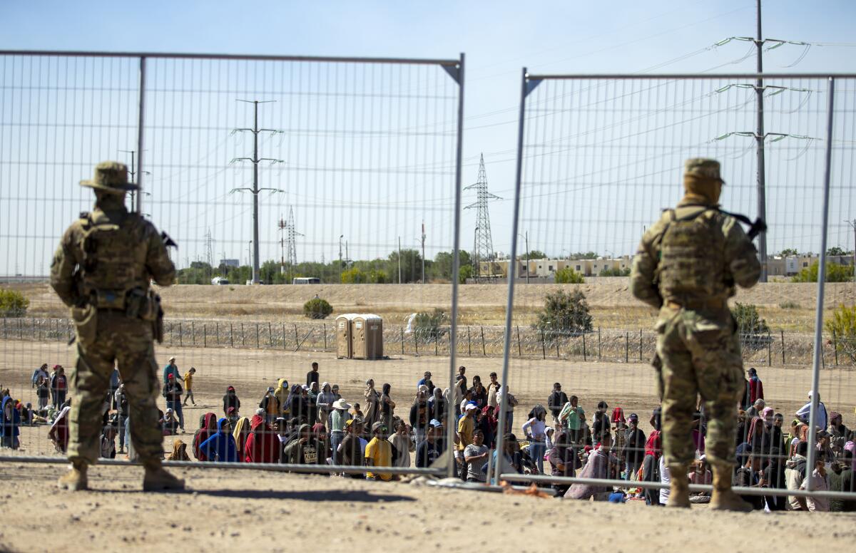ARCHIVO - Migrantes esperan junto a una valla fronteriza bajo la vigilancia de la Guardia Nacional 