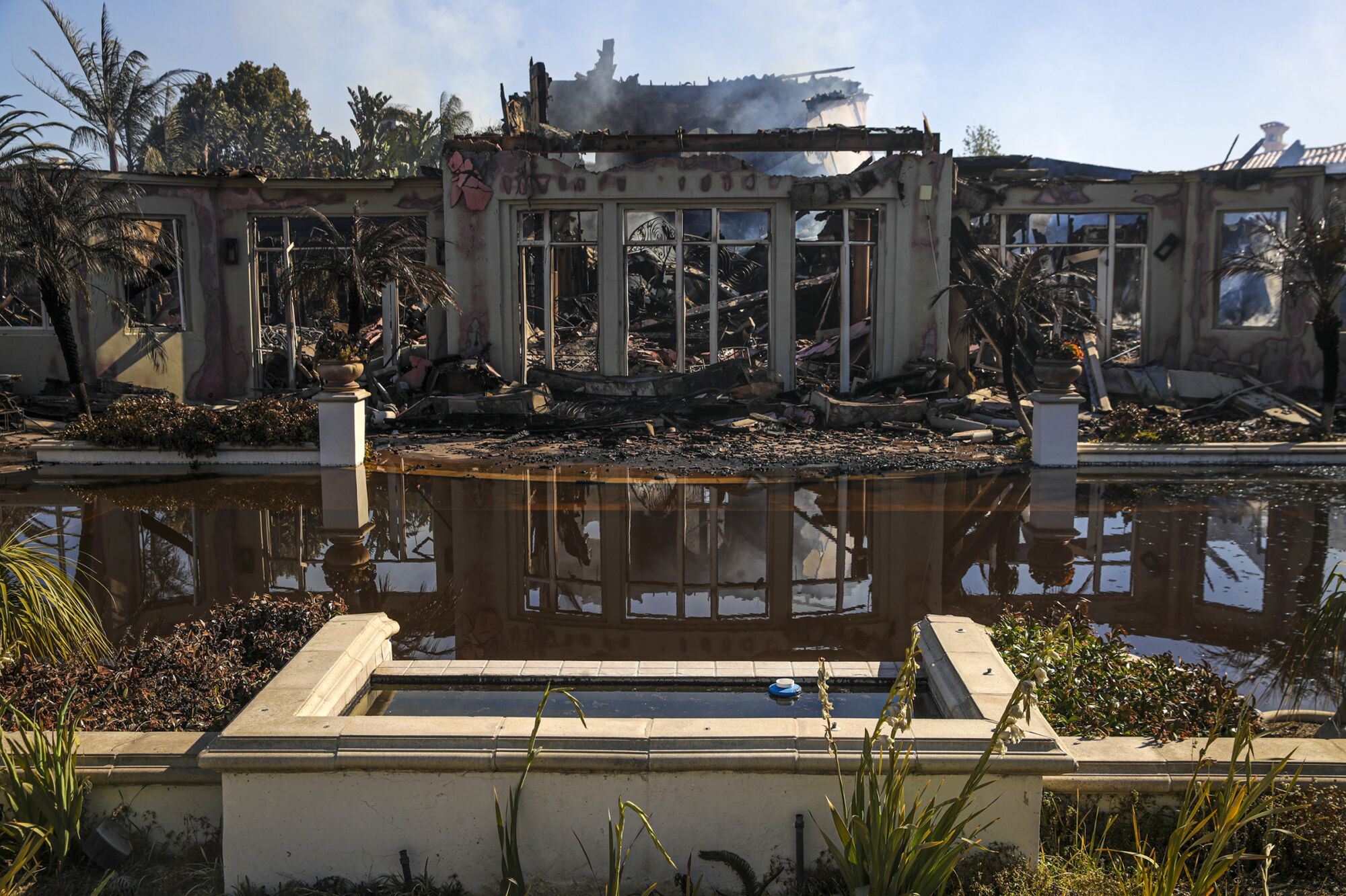 A large home continues to smolder from the Coastal fire on Vista Court in Laguna Niguel.