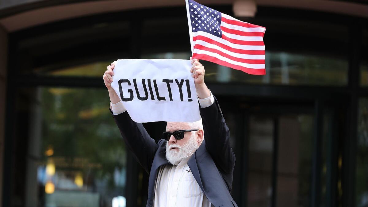 A demonstrator holds up a sign and flag after leaving the courthouse following the verdict announcement Tuesday in the trial of former Trump campaign manager Paul Manafort in Alexandria, Va.