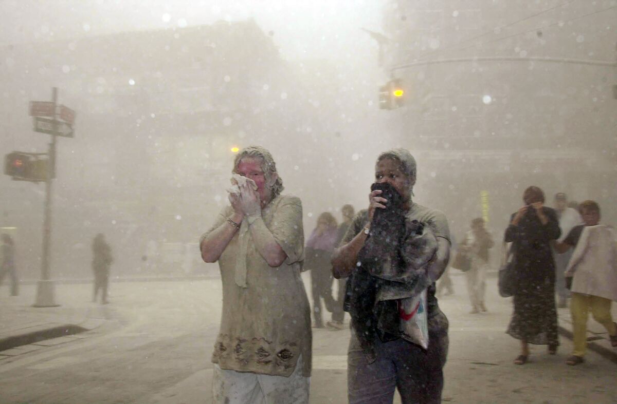 FILE — In this Sept. 11, 2001 file photo, people covered in dust from the collapsed World Trade Center buildings, walk through the area, in New York. Two decades after the twin towers' collapse, people are still coming forward to report illnesses that might be related to the attacks. (AP Photo/Suzanne Plunkett, File)