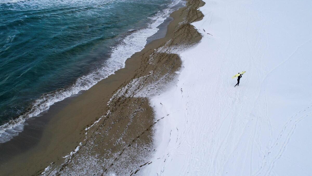 A surfer carries his board as he walks through the snow out of the water in Unstad, Norway.