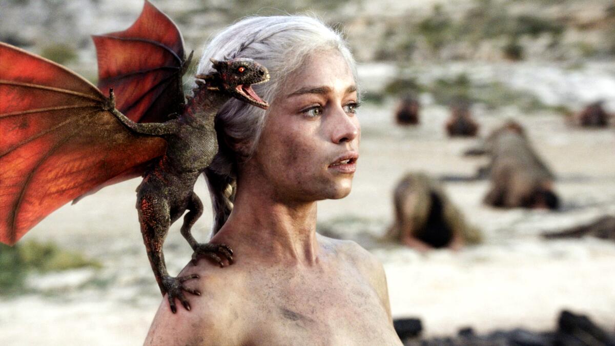 A woman stands with a small dragon on her shoulder.