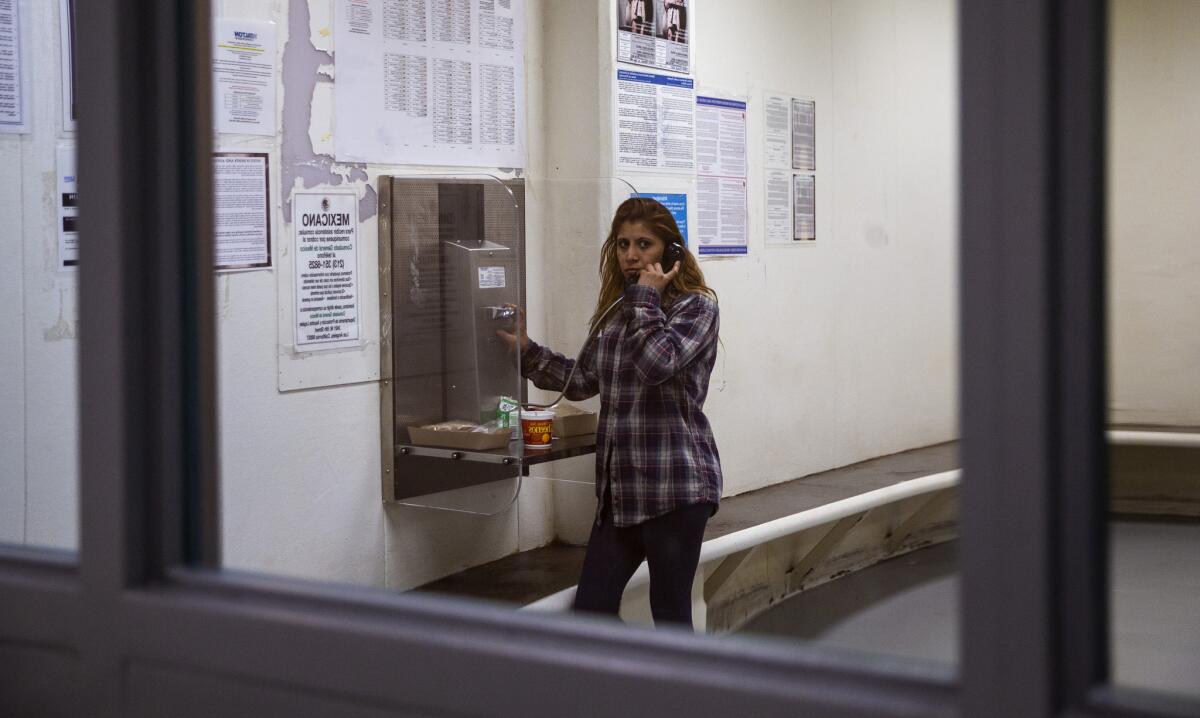 Reflected in the window of the holding area, Adriana Espejel tries to contact the Mexican consulate while being held at the Immigration and Customs Enforcement Los Angeles processing center.
