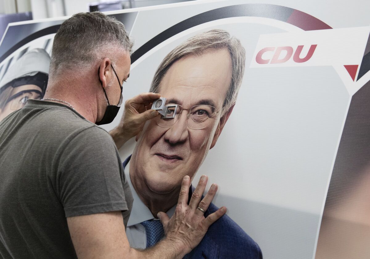 Employee Marc Berenbrinker uses a magnifying glass to check a election poster with a picture of party leader and German Chancellor candidate Armin Laschet in Holte-Stutenbrock, Germany, Tuesday, July 6, 2021. Chancellor Angela Merkel's party on Tuesday presented a campaign for Germany's September election that portrays would-be successor Armin Laschet as an experienced, conciliatory leader and mixes classic center-right themes with an attempt to show fighting climate change as an economic opportunity. (Friso Gentsch/dpa via AP)
