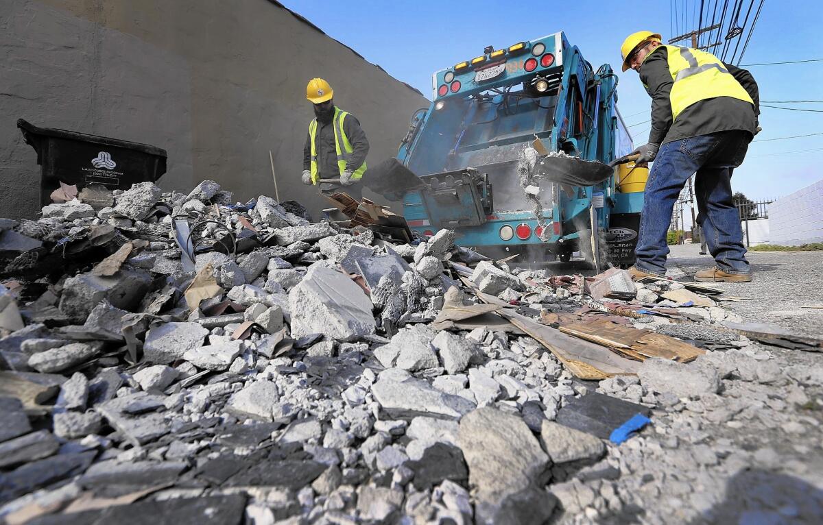 Octavio Mojarro, left, and Jakub Nademlynsky, who work for the city of Los Angeles, clean construction debris illegally dumped in a Mid-City alley last week.
