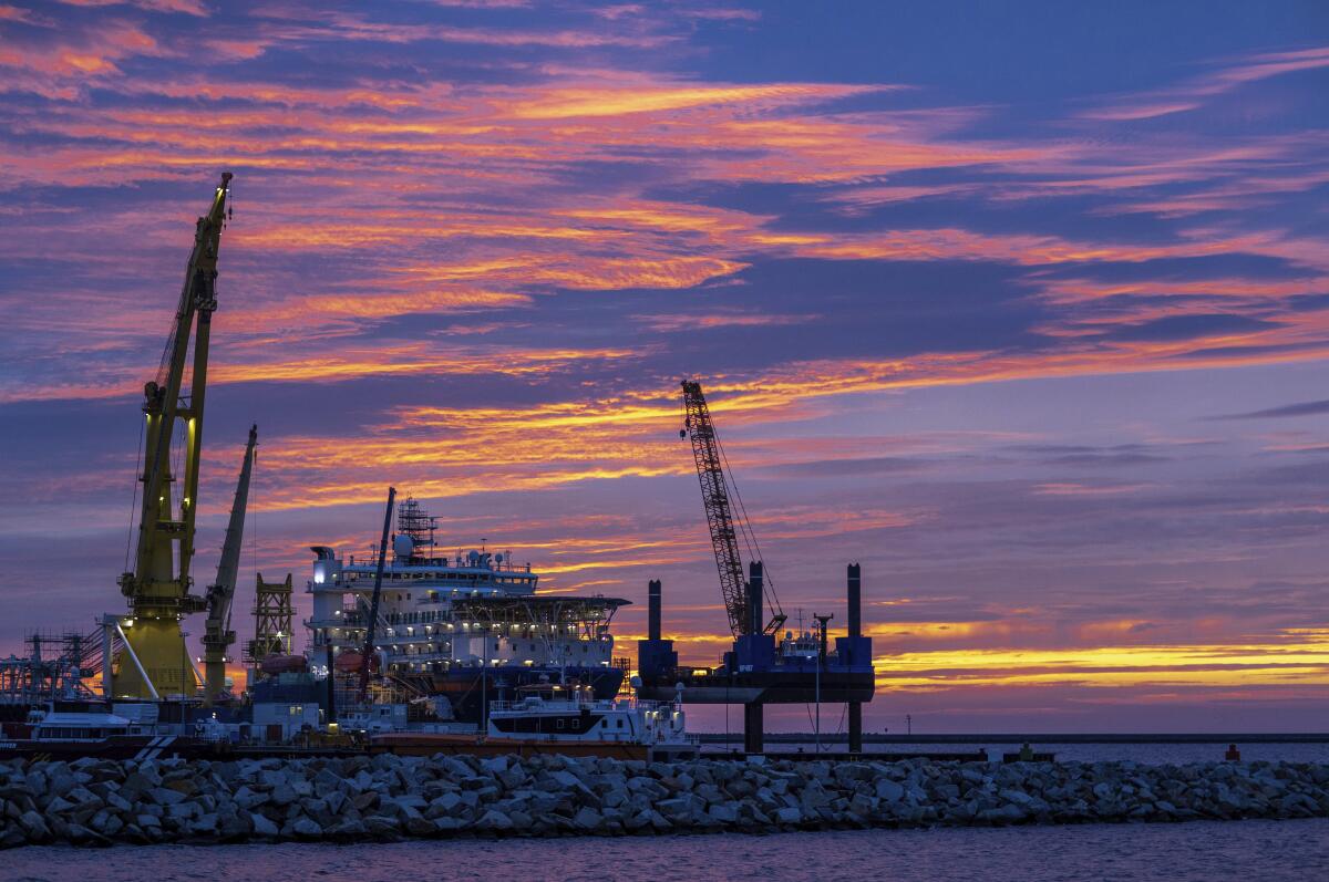A ship is shown between two cranes on a jetty. A beautiful sunset is in the background.