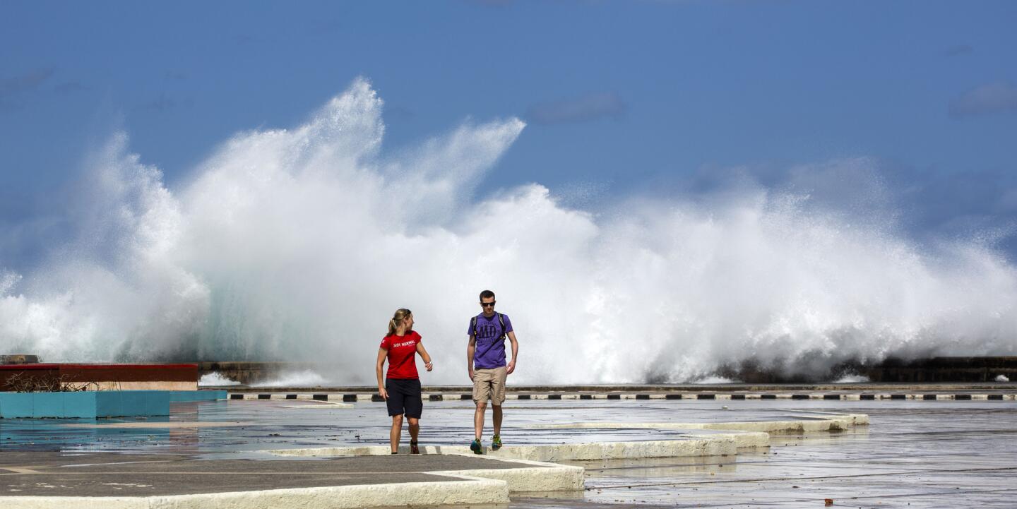 En esta imagen una pareja camina con las olas rompiendo de fondo en el Malecón de La Habana, Cuba. (AP Foto/Desmond Boylan)