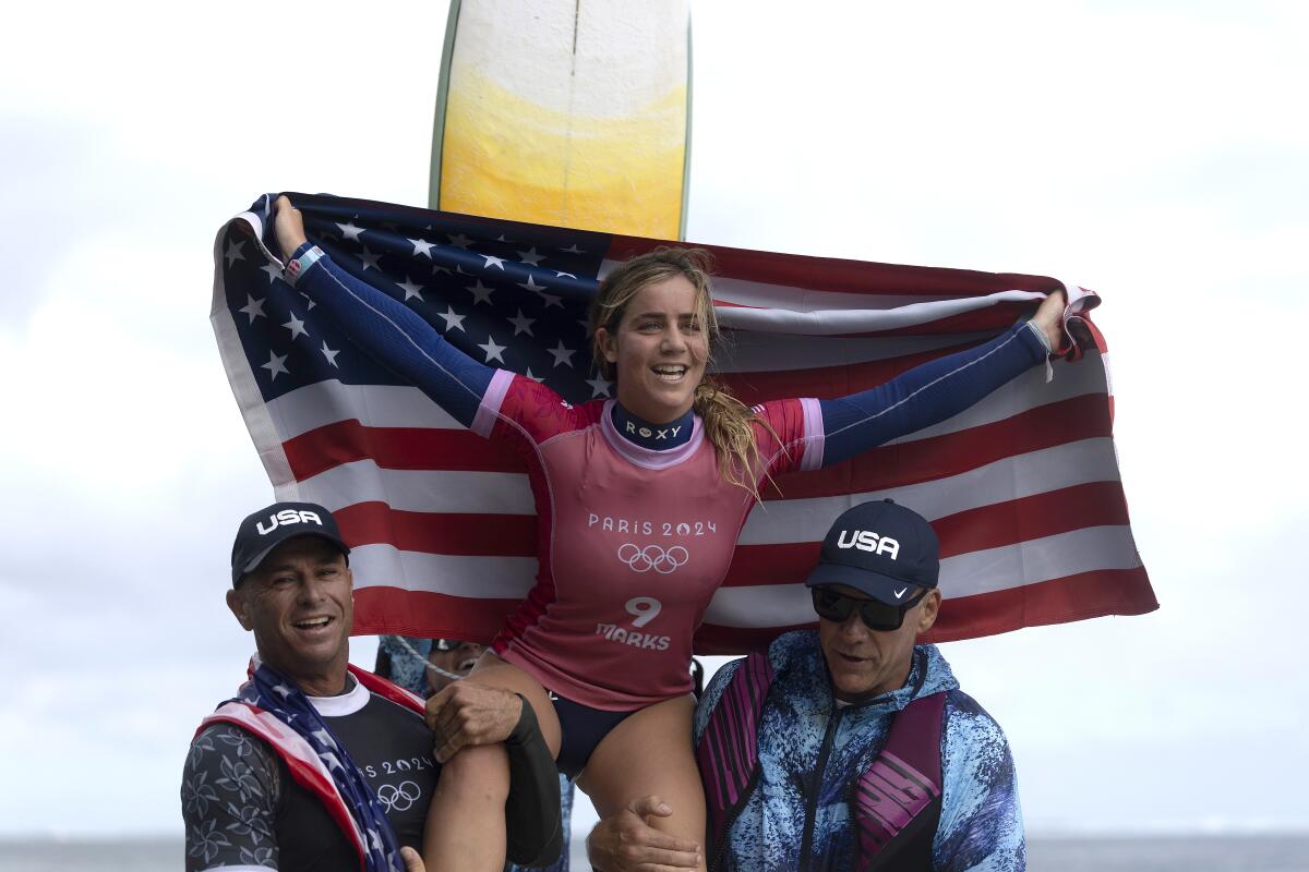 American Caroline Marks holds a U.S. flag and cheers as she is carried to the podium after winning women's surfing 