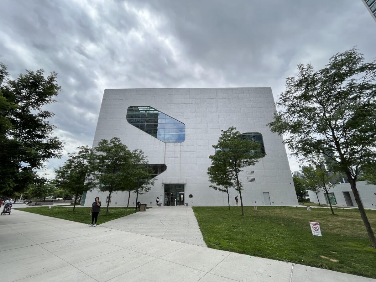 The white facade of the Hunters Point library, with its irregularly shaped windows, is visible against a cloudy sky