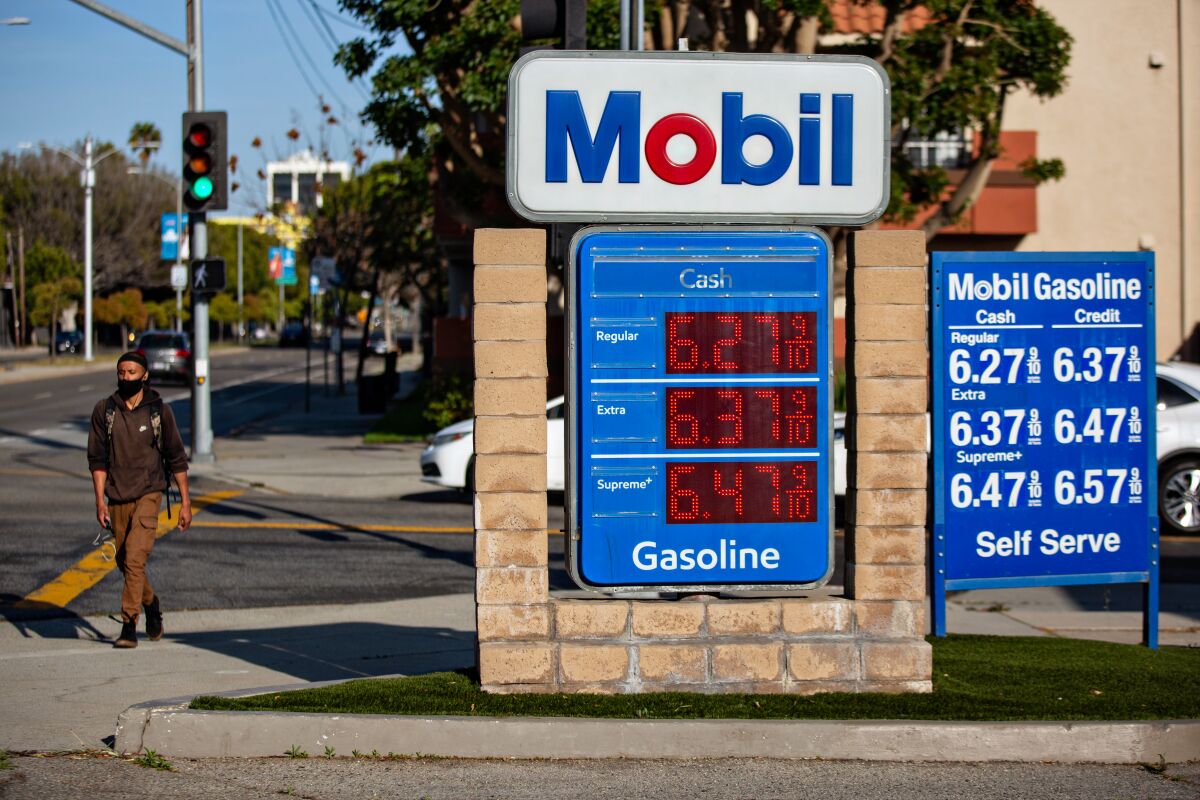 A man walks on the sidewalk beside a sign advertising gas prices at a Mobil station