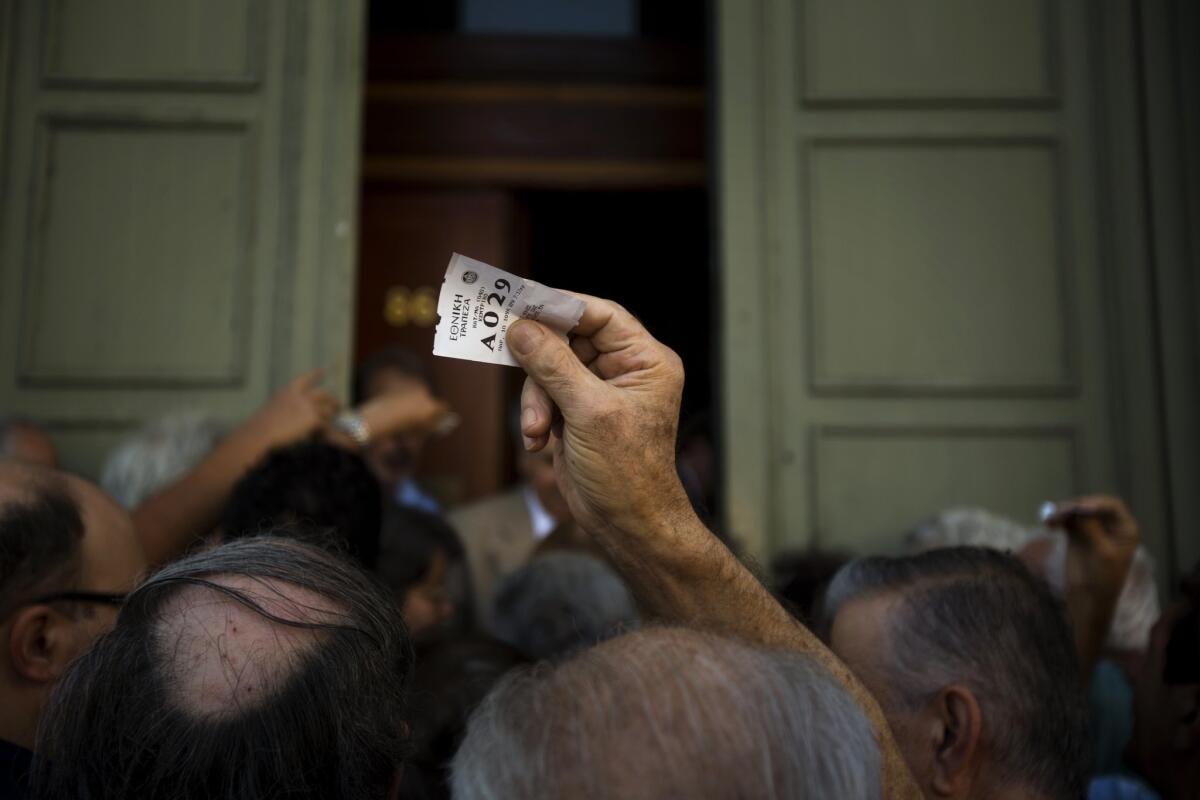 A man holds a tag showing his position in line as he waits Friday with other retirees outside the National Bank of Greece in Athens to withdraw funds.
