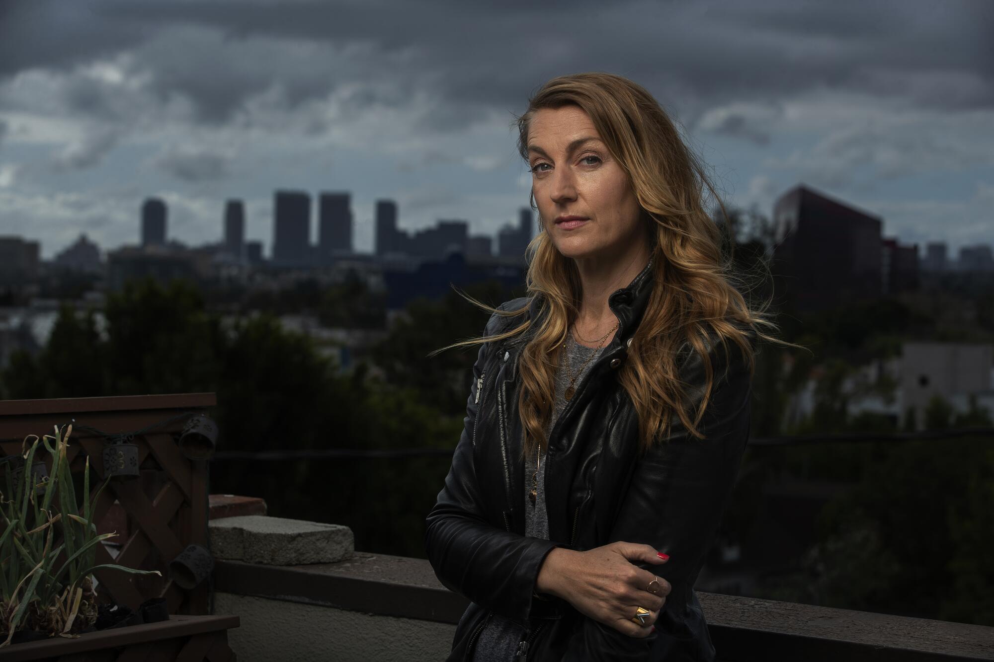 A woman crosses her arms while posing for a portrait with a city skyline in the background