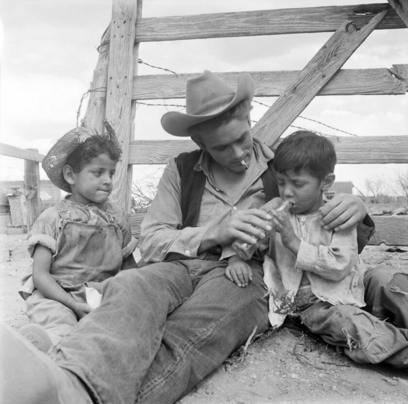 James Dean sitting next to a corral with two kids on the set of the movie "Giant" 