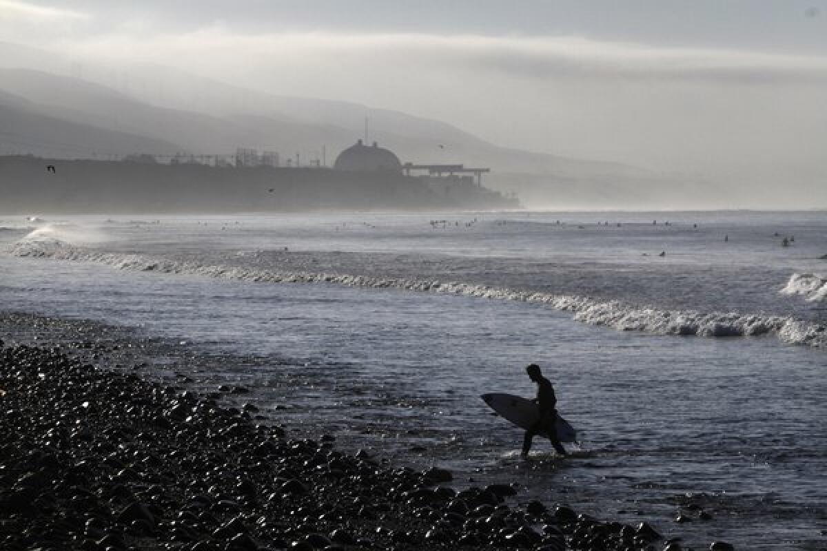 Early morning surfers catch a few waves while a fog bank clears away at Lower Trestles in San Clemente with the San Onofre power plant in the background.