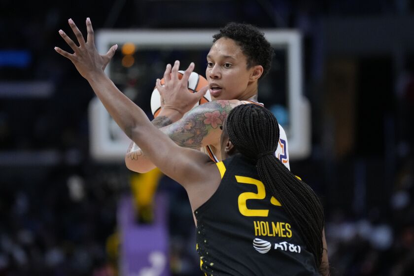 Mercury center Brittney Griner holds up the ball while Sparks player Joyner Holmes raises her arm to block Griner's view