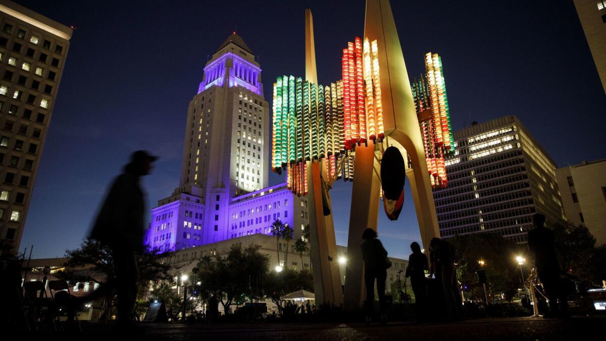 People walk past the Triforium illuminated with LED lights as part of a restoration effort as City Hall stands illuminated in the background.
