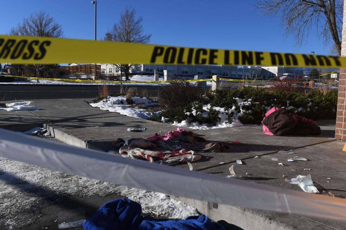 Snow and bloodstained clothes on the sidewalk behind police tape.