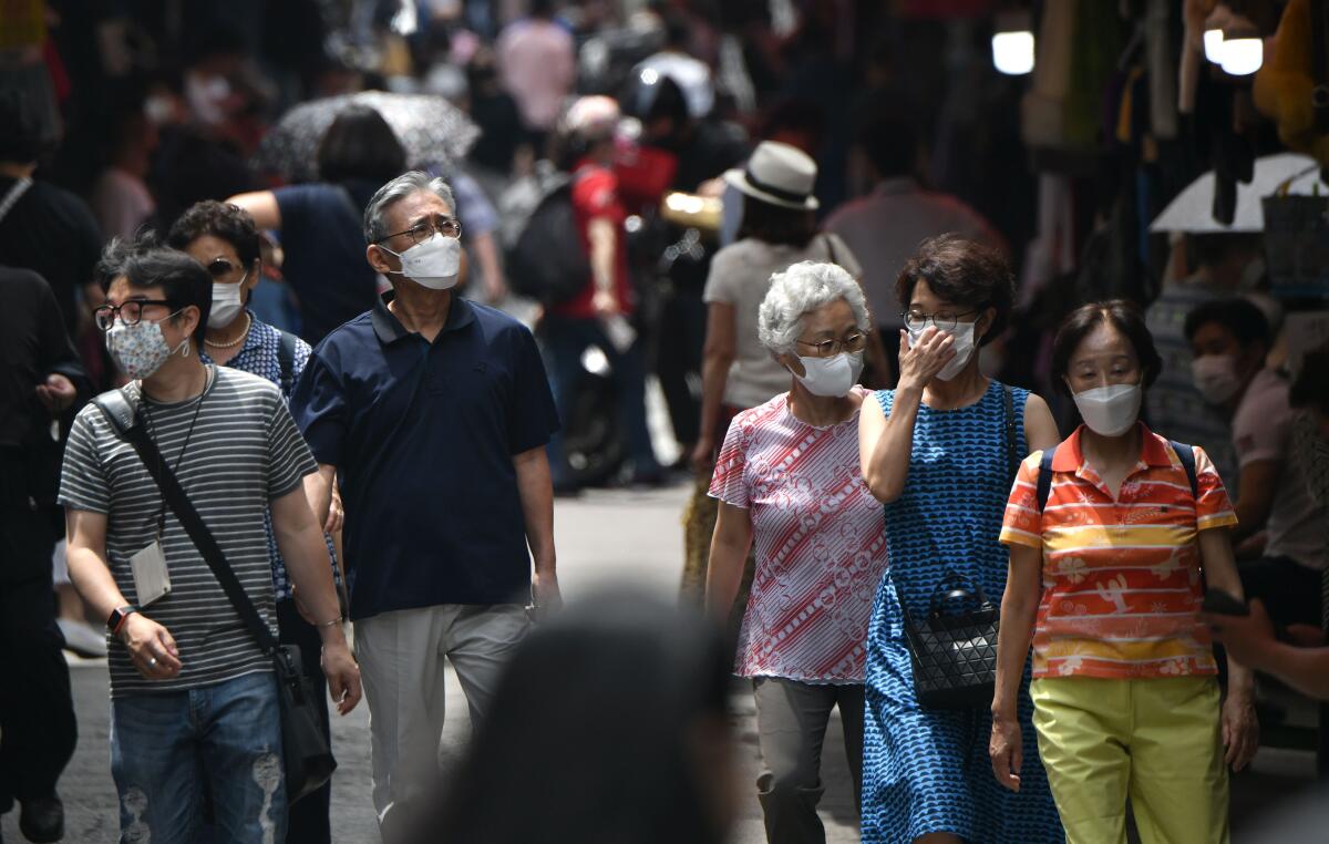 Pedestrians wearing masks walk through a market in Seoul. 