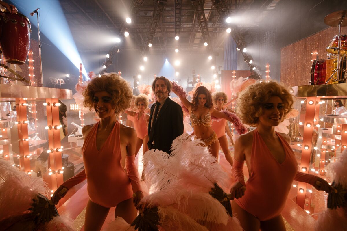 A man in a coat and tie stands amid dancers in a club