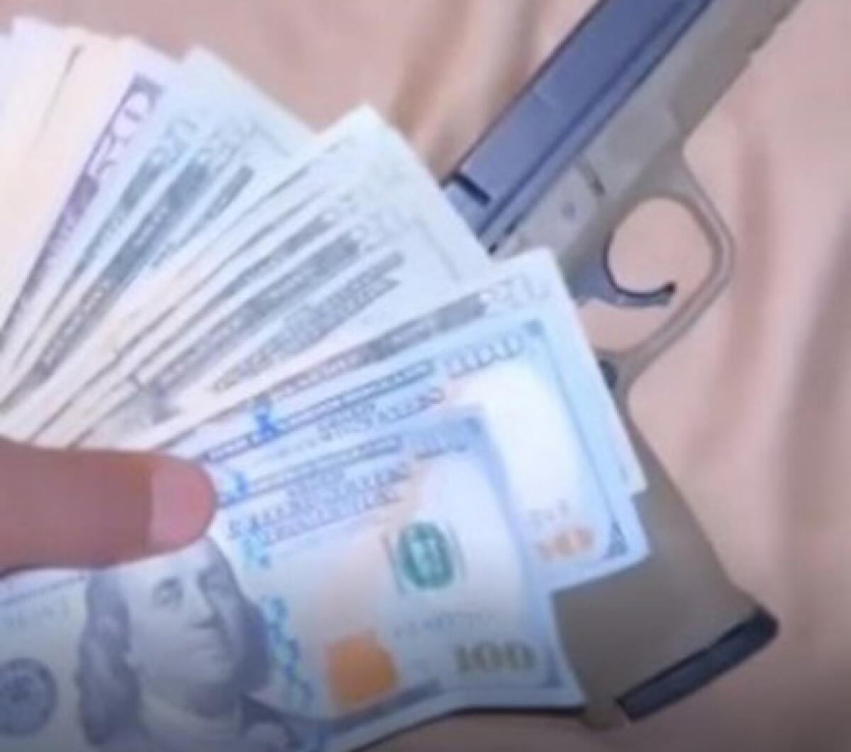A closeup of a gun and a hand holding cash.