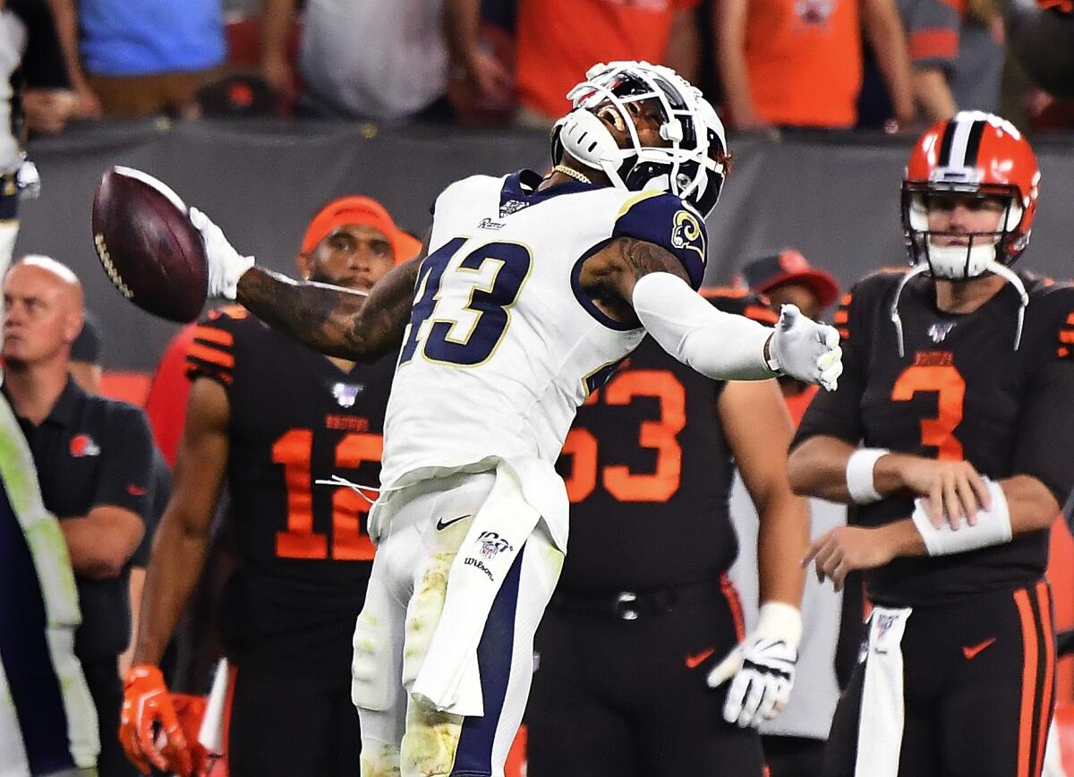 Rams safety John Johnson holds a football and looks up while opponents stand behind him on the field.