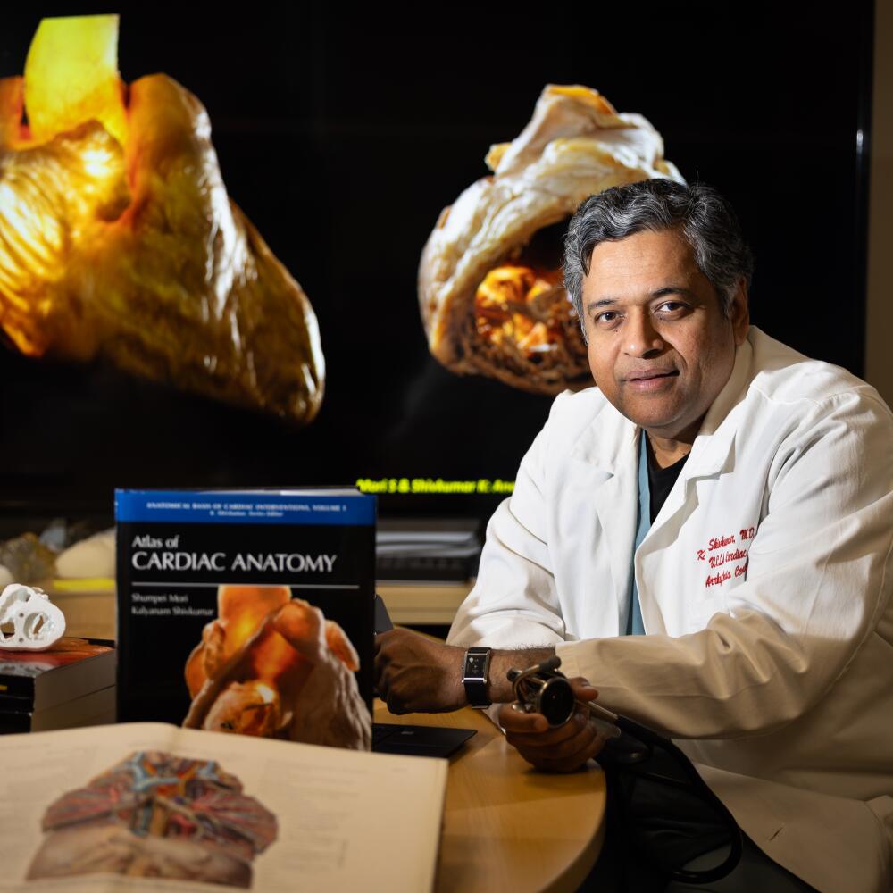Dr. Kalyanam Shivkumar of UCLA at a table with books. Large images of hearts are behind him.