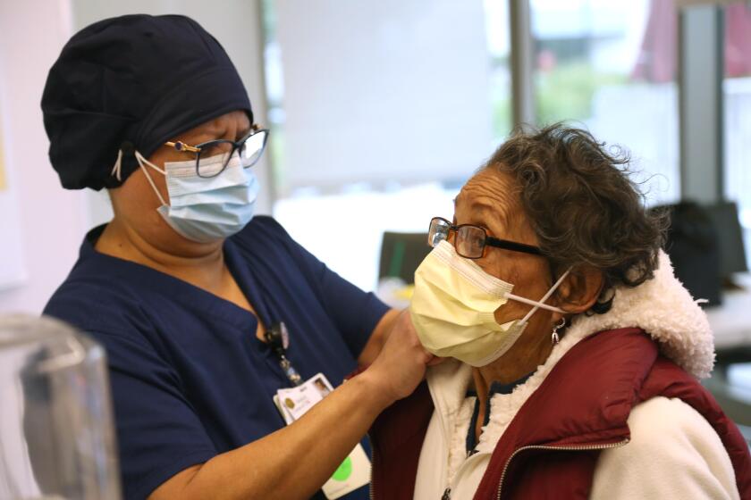 LOS ANGELES, CA - JANUARY 23, 2021 - Maria Saravia, left, an Environmental Services Worker at Keck Hospital of USC, tightens the mask of her mother Sara Saravia, 81, before Sara receives the vaccine against COVID-19 at Keck Medicine of USC in Los Angeles on January 23, 2021. Keck began vaccinating family members, who are 65 and older, of staff that included hospital housekeepers, valet and cafeteria workers. (Genaro Molina / Los Angeles Times)