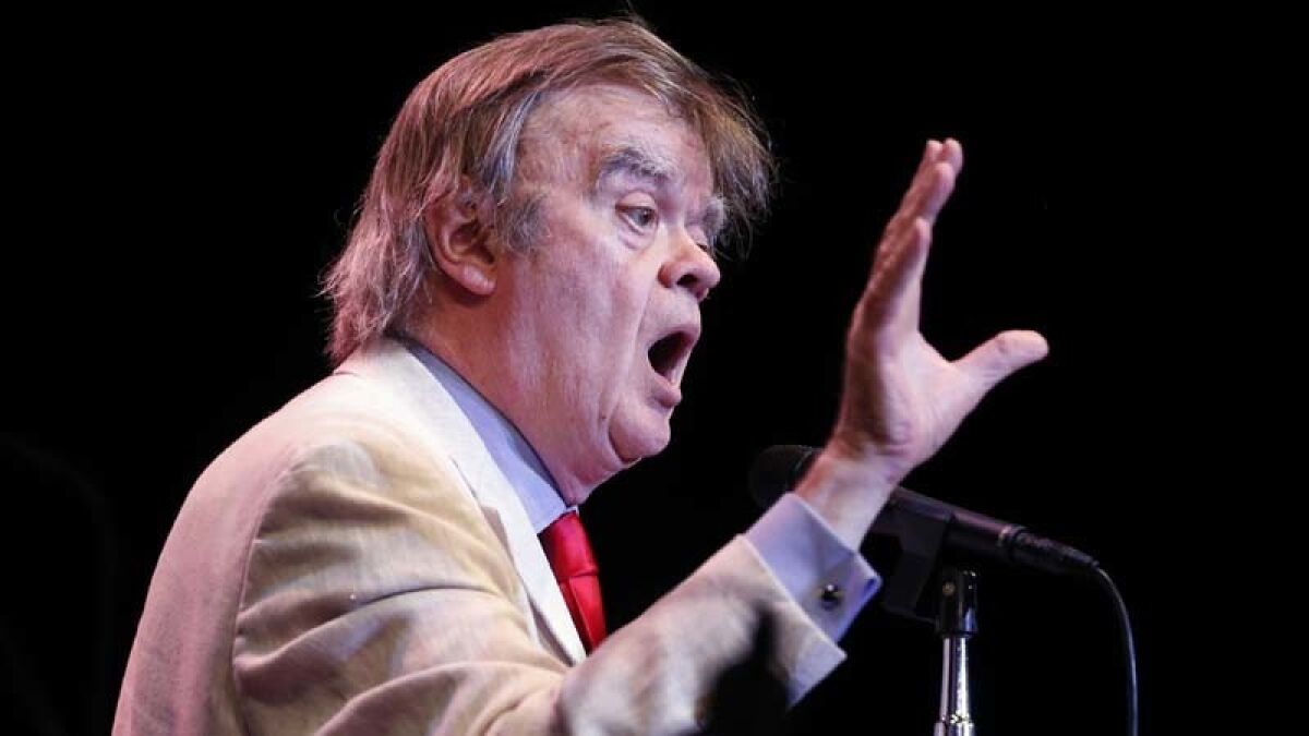 Garrison Keillor speaks into a microphone on stage.