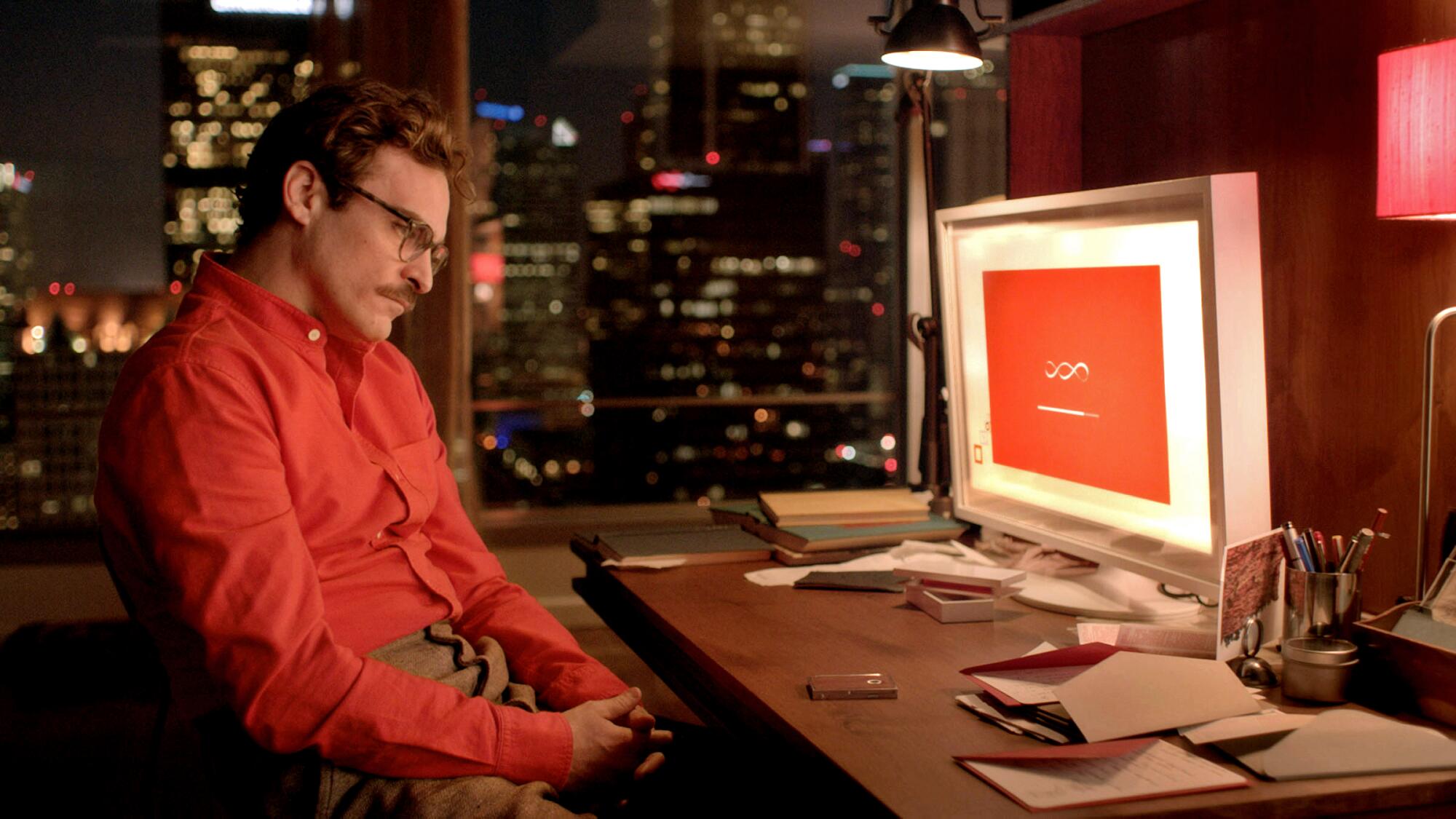 Joaquin Phoenix dans le rôle de Théodore dans le film "Son," assis au bureau de l'ordinateur. 