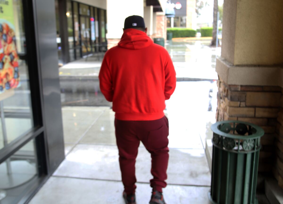 A man in a red hoodie walks to his car, with his back to the camera.