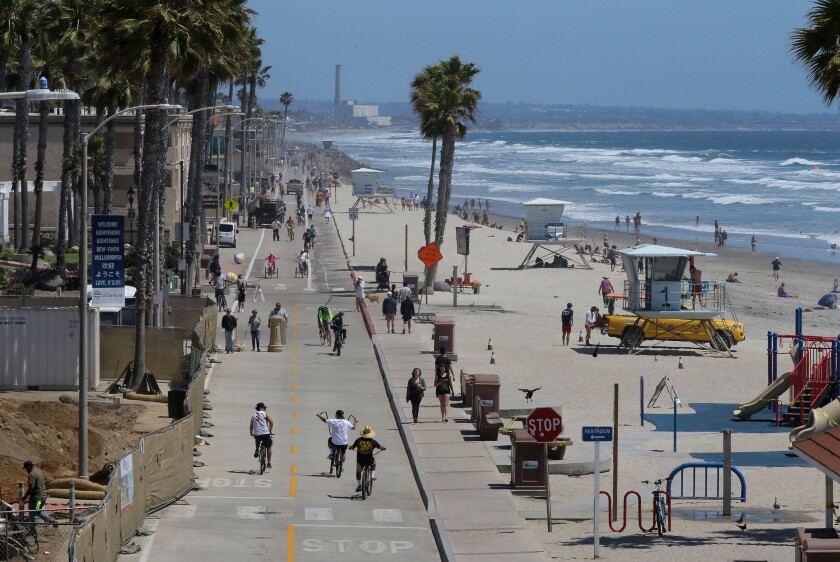 People walk along The Strand and the beach south of the Oceanside Pier in May 2020. 