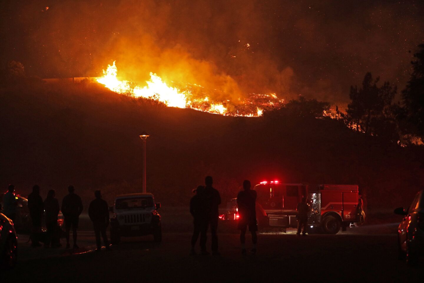 A crowd watches a hillside burn