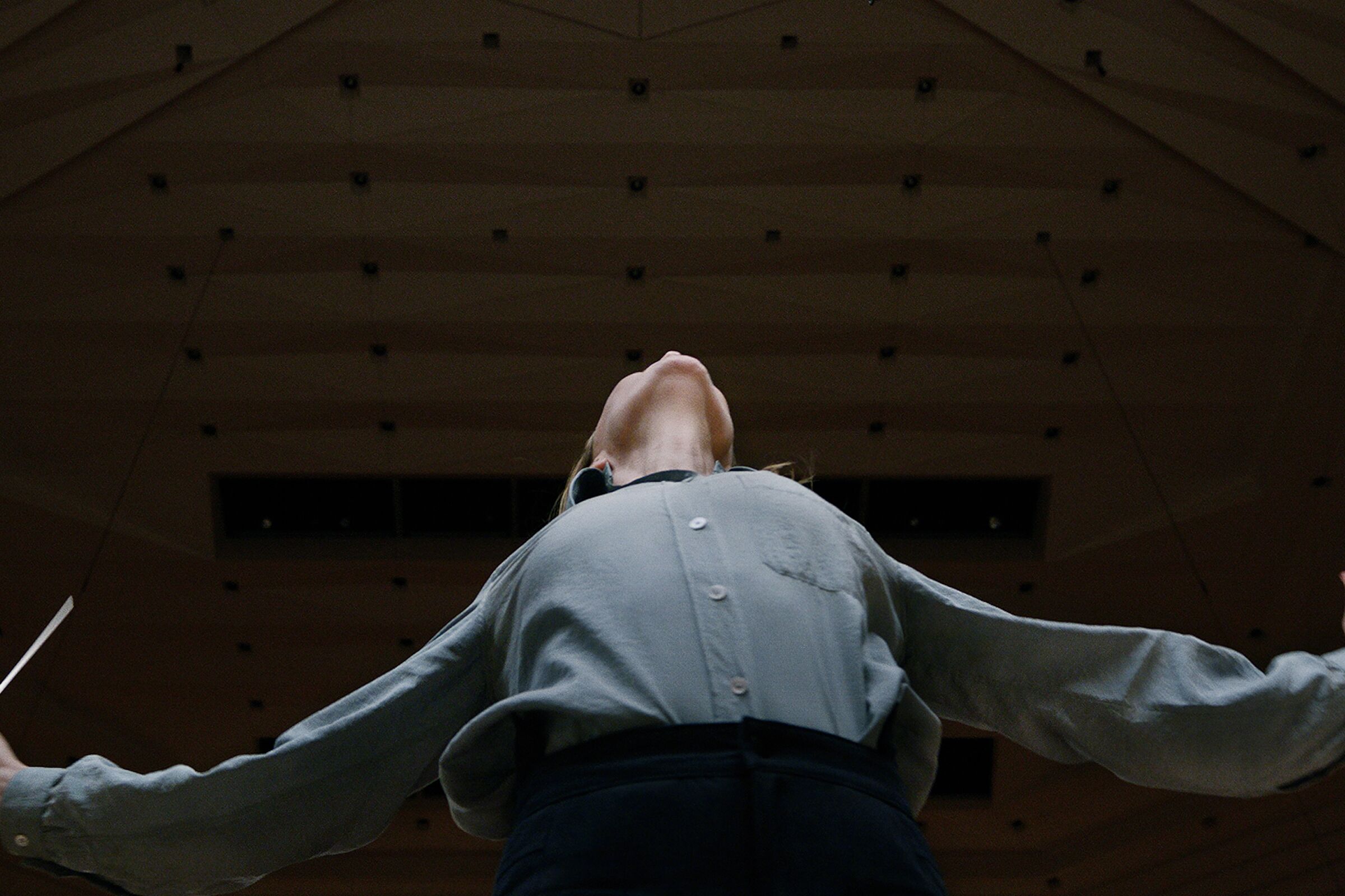 A woman conductor looks toward the ceiling, as seen from the floor below her looking up.