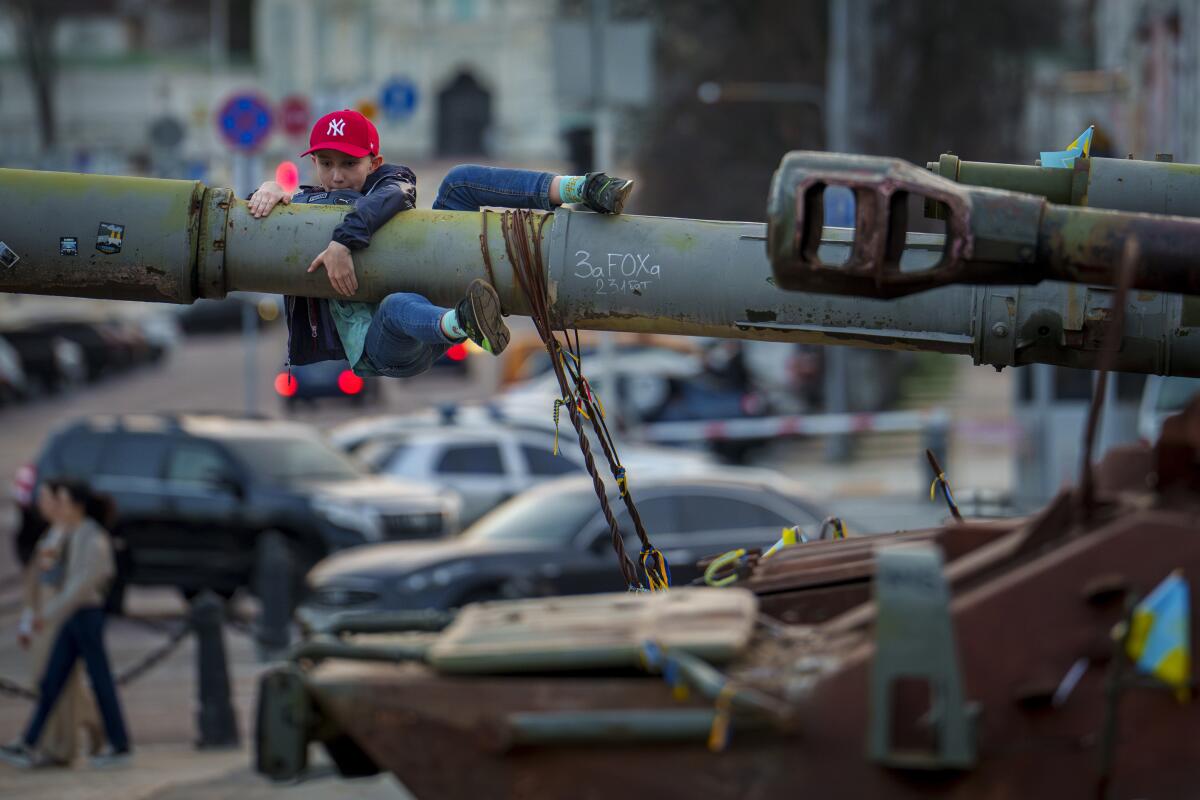 A boy holds on to the barrel of a tank, part of a display of destroyed Russian military equipment.