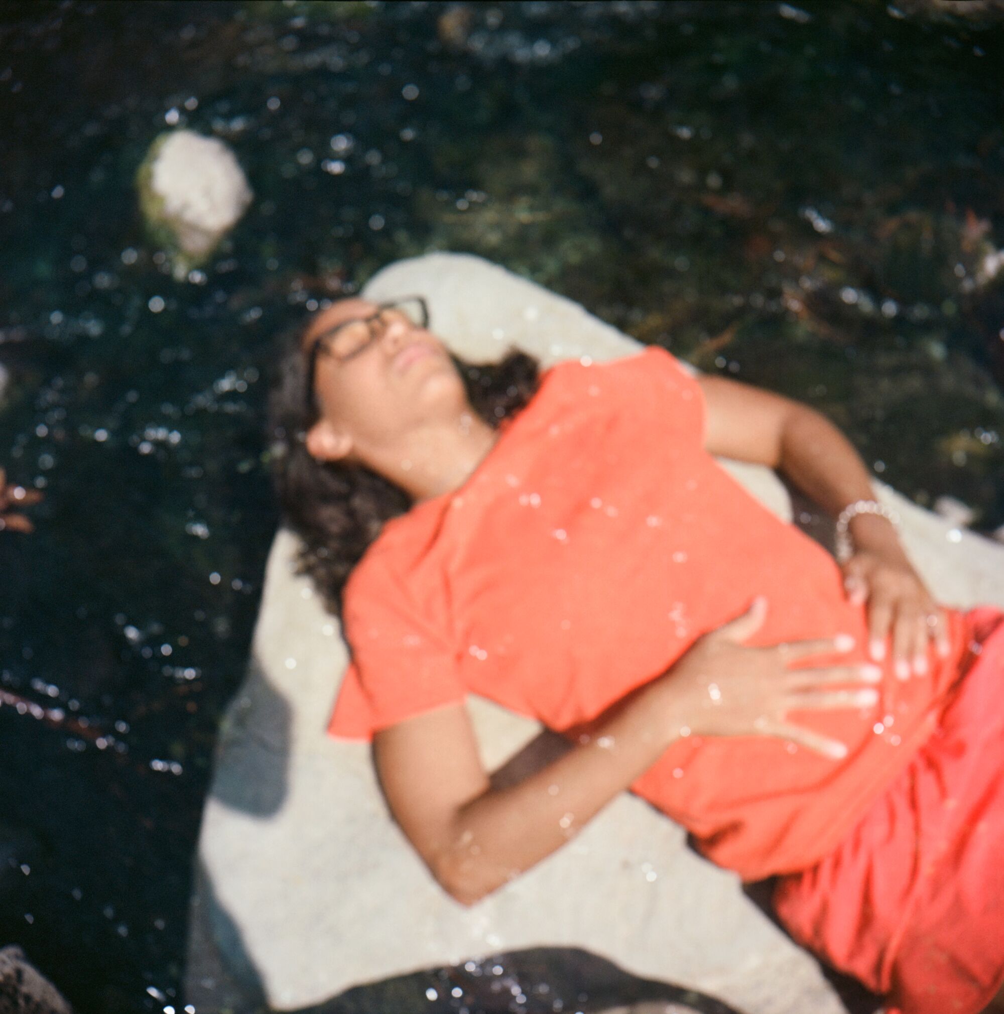 An out-of-focus view of Lacey Lennon lying on a rock surrounded by water.