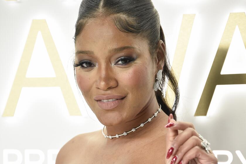 Keke Palmer in a blue patterned dress holding up her left hand