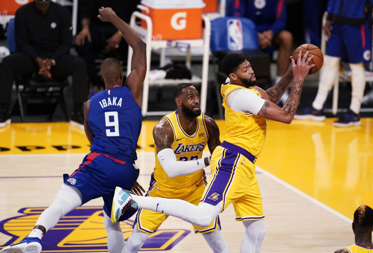 Lakers forward Anthony Davis grabs a rebound next to teammate LeBron James and Clippers center Serge Ibaka (9) on Tuesday.