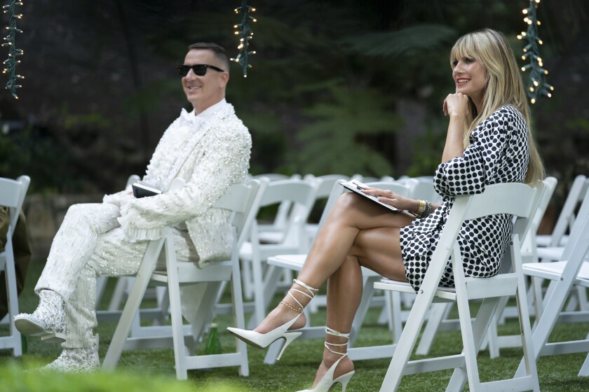 A man and a woman seated outdoors among a group of white folding chairs