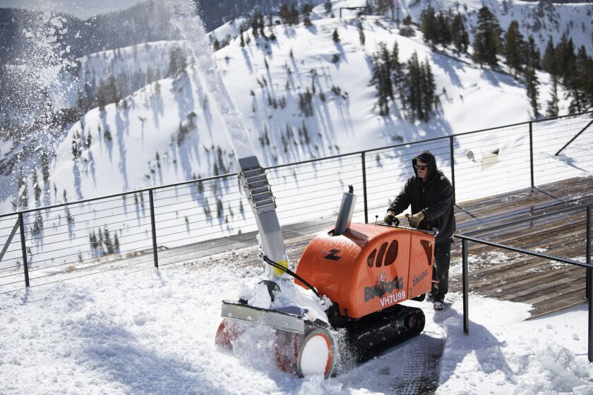 A worker clears the deck of snow after a Spring storm at the top of the aerial tram at Palisades Tahoe.