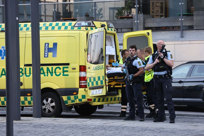 Armed police officers stand at the open back of an ambulance.