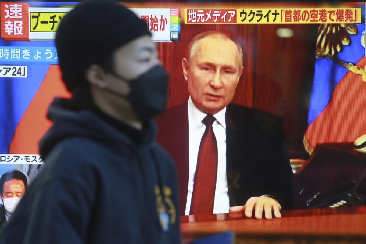 A man wearing a mask walks past a TV screen with an image of Russian President Vladimir Putin on it