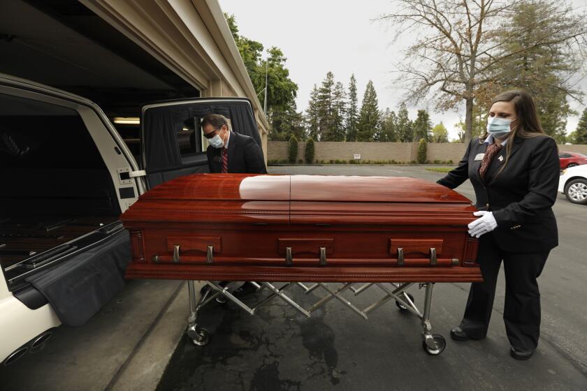 MADERA, CALIFORNIA-APRIL 8, 2020-Jay Chapel funeral director Sarah Smith, right, and another member of Jay Chapel Funeral Home use strict protocol to handle victims of Covid-19 coronavirus. They prepare to take a victim to the cemetery on April 8 2020. (Carolyn Cole/Los Angeles Times)