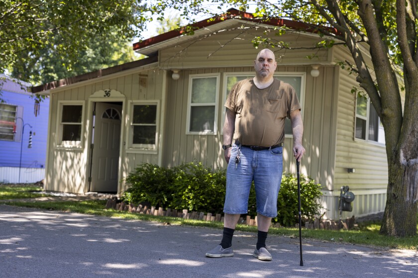A man with a cane stands in front of his mobile home.