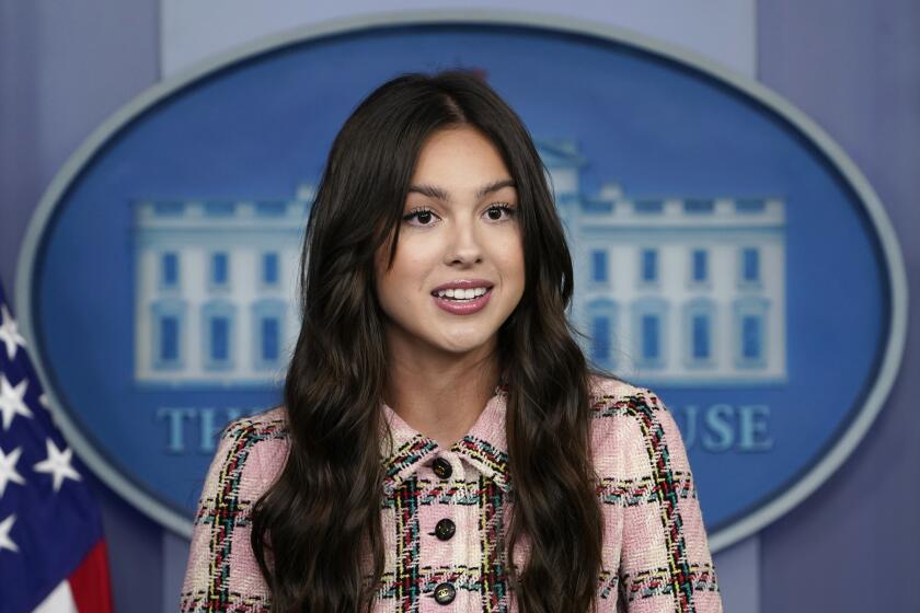 A young woman with long, brown hair speaking in front of the White House seal