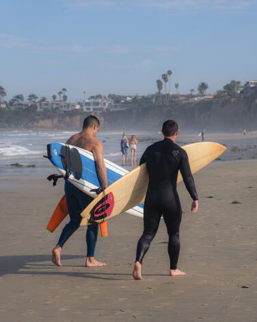 Surfers walk with their boards at Tourmaline Canyon in San Diego, California. Photographed in June 2024.