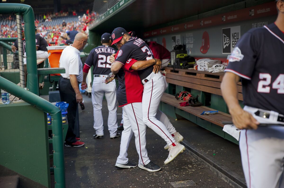 In this May 4, 2018, photo, Washington Nationals Bryce Harper is hugged and lifted off the ground by his manager Dave Martinez in the dugout prior to the start of a baseball game against the Philadelphia Phillies at Nationals Park in Washington. High fives and fist bumps are out. Hugs are a no-go. And just like crying, there's no spitting in baseball, at least for now. Things sure will be different when it's time to play ball in two weeks. (AP Photo/Pablo Martinez Monsivais, File)