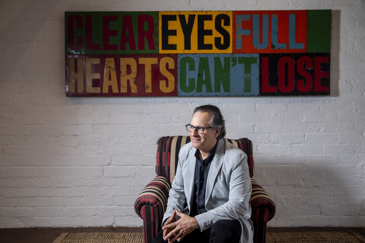 Jason Katims beneath a piece of wall art that reads: "Clear eyes full hearts can't lose."