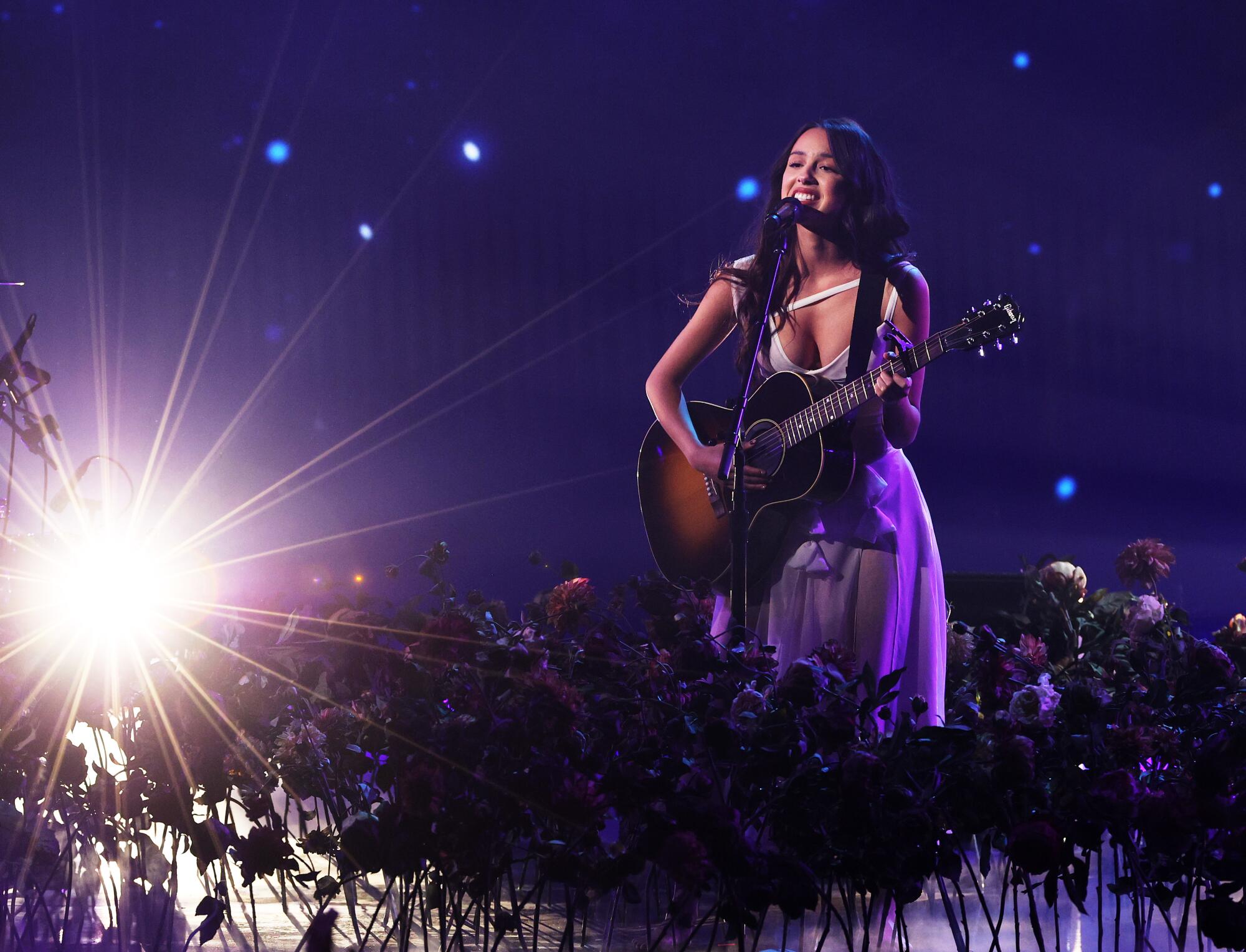 A young woman with an acoustic guitar performs onstage.